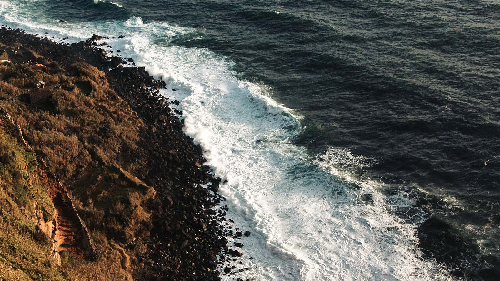 Captured from above, ocean waves gently break onto a beach covered with rocks.