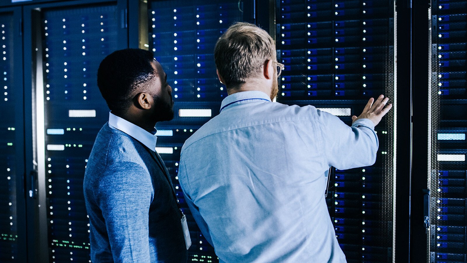 Close-up of two male persons seen from behind when inspecting data center cabinets.