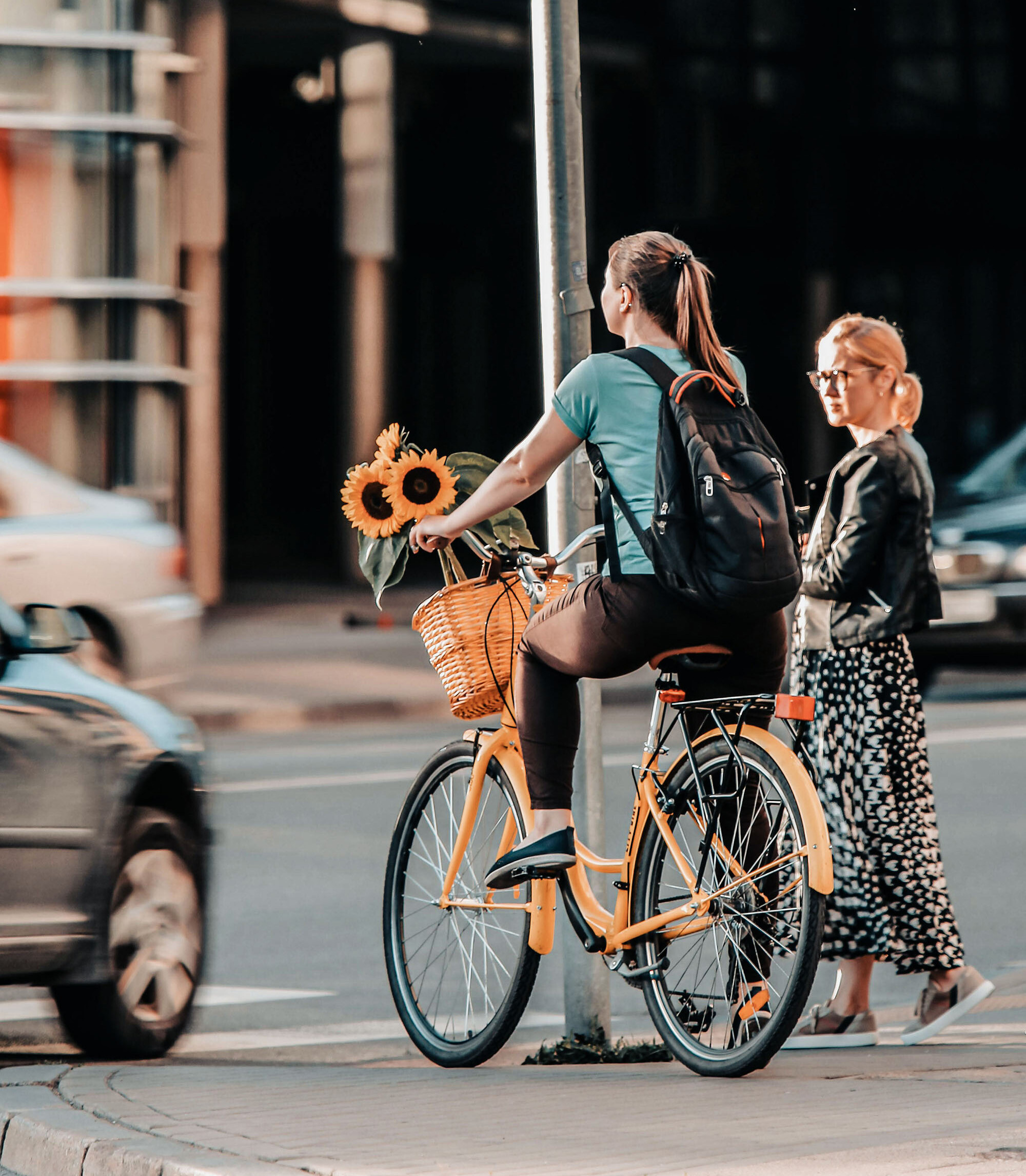 A woman with her bike is waiting at a pedestrian crossing for a car to drive past.