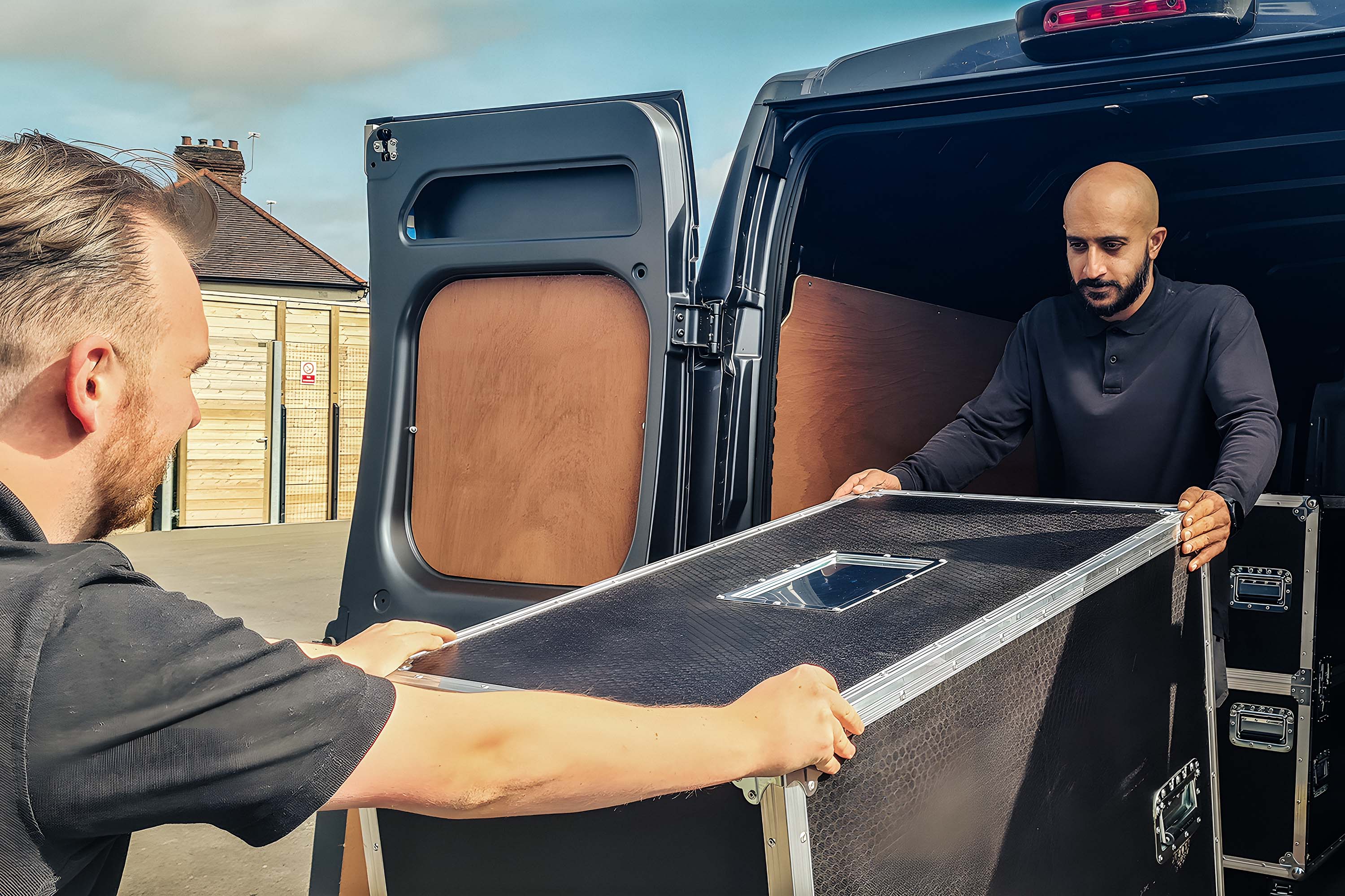 Two engineers are unloading a large box from the back of a van.