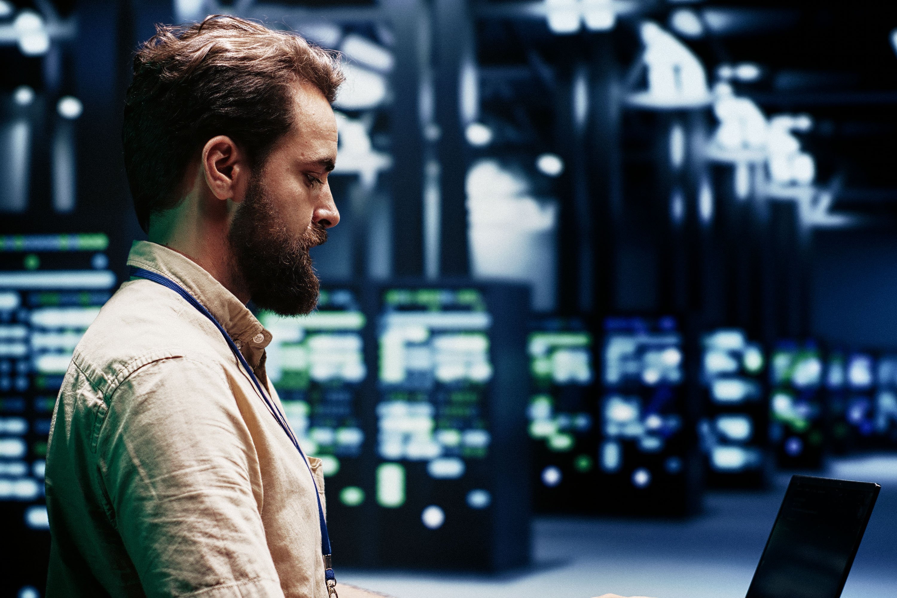 Man working on a computer in a data center. The background is blurry. 