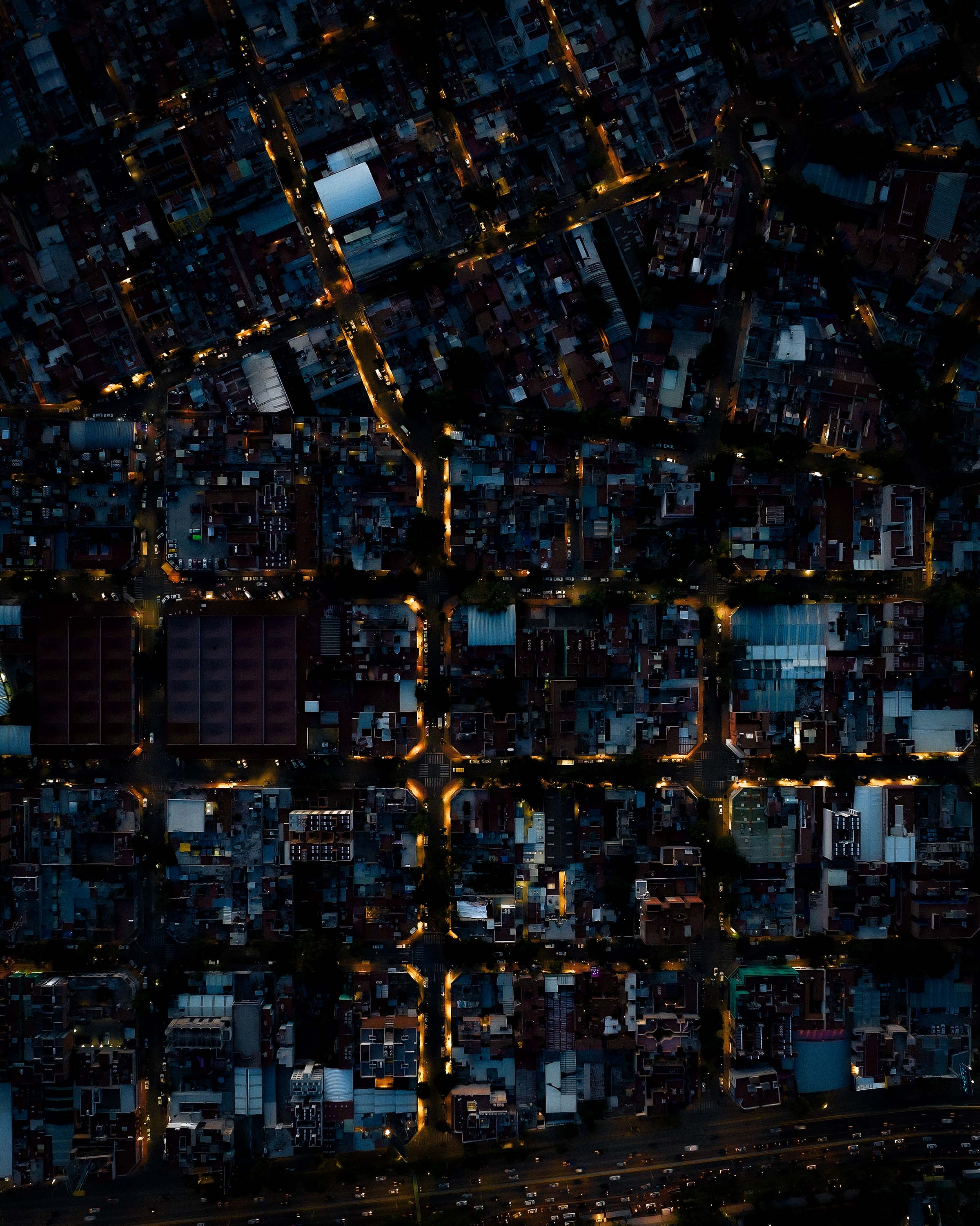 A drone view of a city at night time. A grid of streets and light below. 
